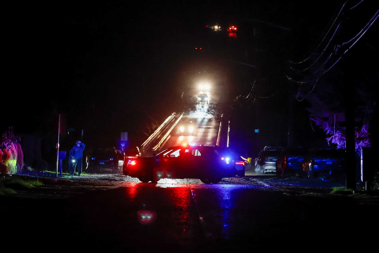 A neighbor looks up the street as a police car blocks 15th Ave NE after trees fell across the road and took down power lines in the Maple Leaf neighborhood during a major storm Tuesday, Nov. 19, 2024 in Seattle. (Jennifer Buchanan/The Seattle Times via AP)