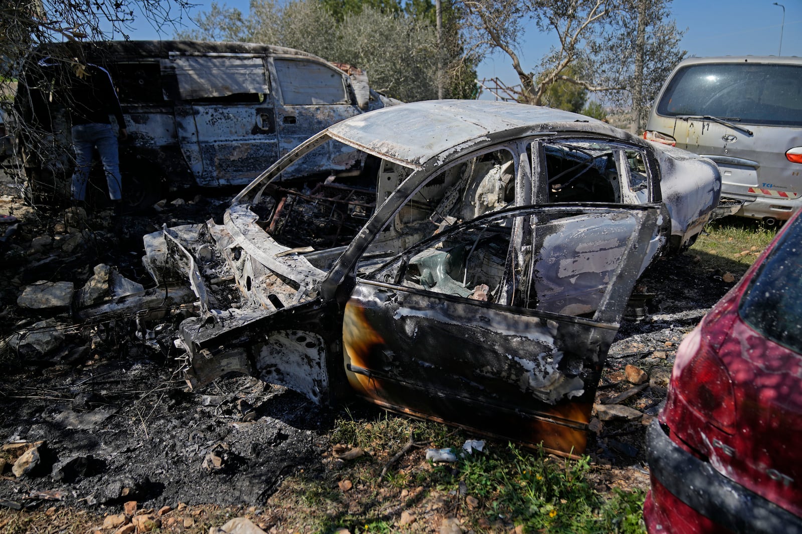 A man inspects a torched vehicle, one of three that were set on fire by attackers overnight in a Palestinian garage in the West Bank village of Umm Safa, north of Ramallah, Tuesday, March 11, 2025. (AP Photo/Nasser Nasser)