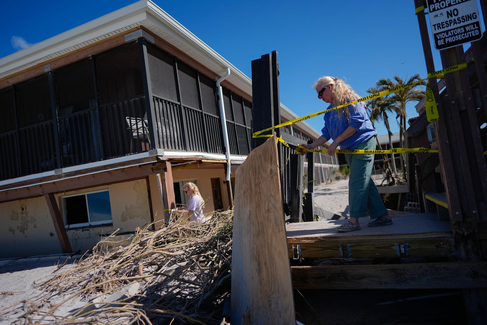 Theresa Carrithers, property manager of Sea Oats Beach Club, puts up caution tape around the hotel's damaged infrastructure, following the passage of Hurricane Milton, on Manasota Key in Englewood, Fla.,, Sunday, Oct. 13, 2024. (AP Photo/Rebecca Blackwell)