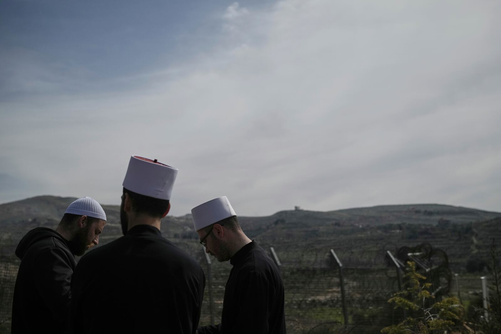 Druze men stand near the border, as they wait for buses carrying members of the Syrian Druze community to cross from Syria in the village of Majdal Shams, located in the Israeli-controlled Golan Heights, Friday, March 14, 2025. (AP Photo/Leo Correa)