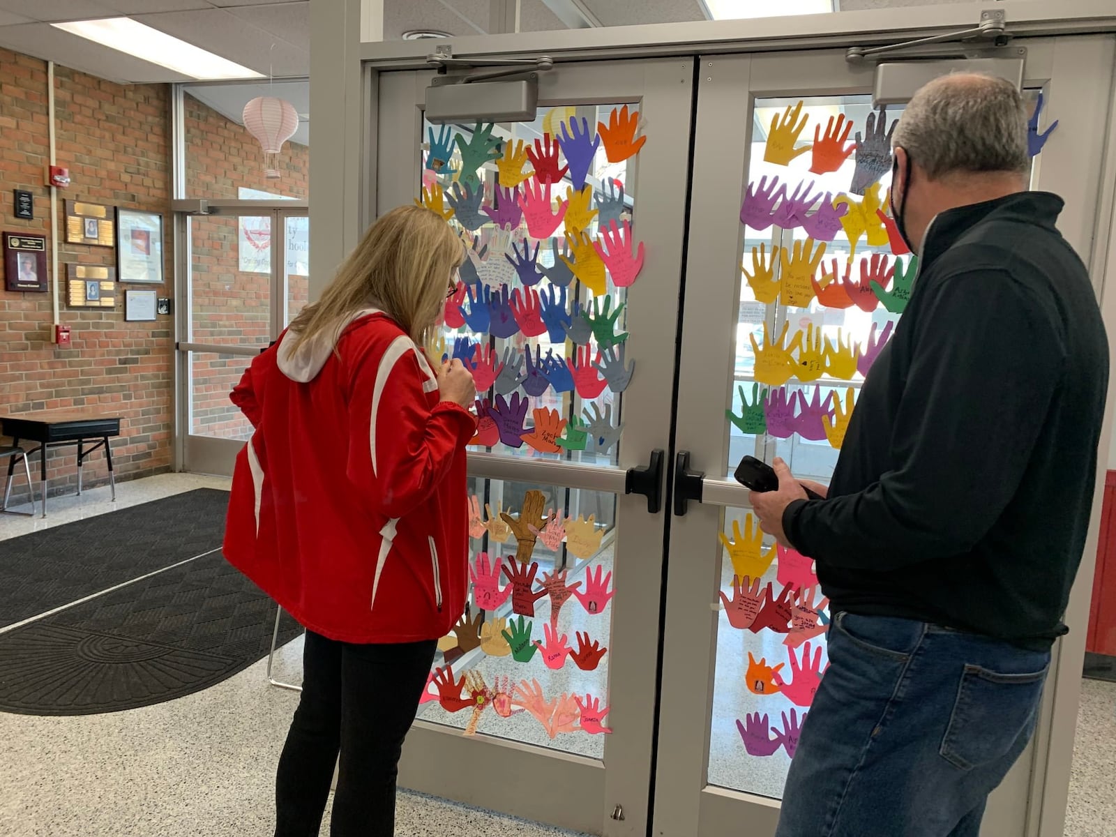 Fairfield West Elementary Principal Missy Muller was recently pleasantly shocked  when her school's nearly 800 students decorated the front lobby and office windows with paper cut outs of their hands adorned with emotional messages of support. Muller - left, reading some of the many messages - is battling a bone marrow disease and is leaving the city - and her job - temporarily for treatment. (Provided Photo\Journal-News)