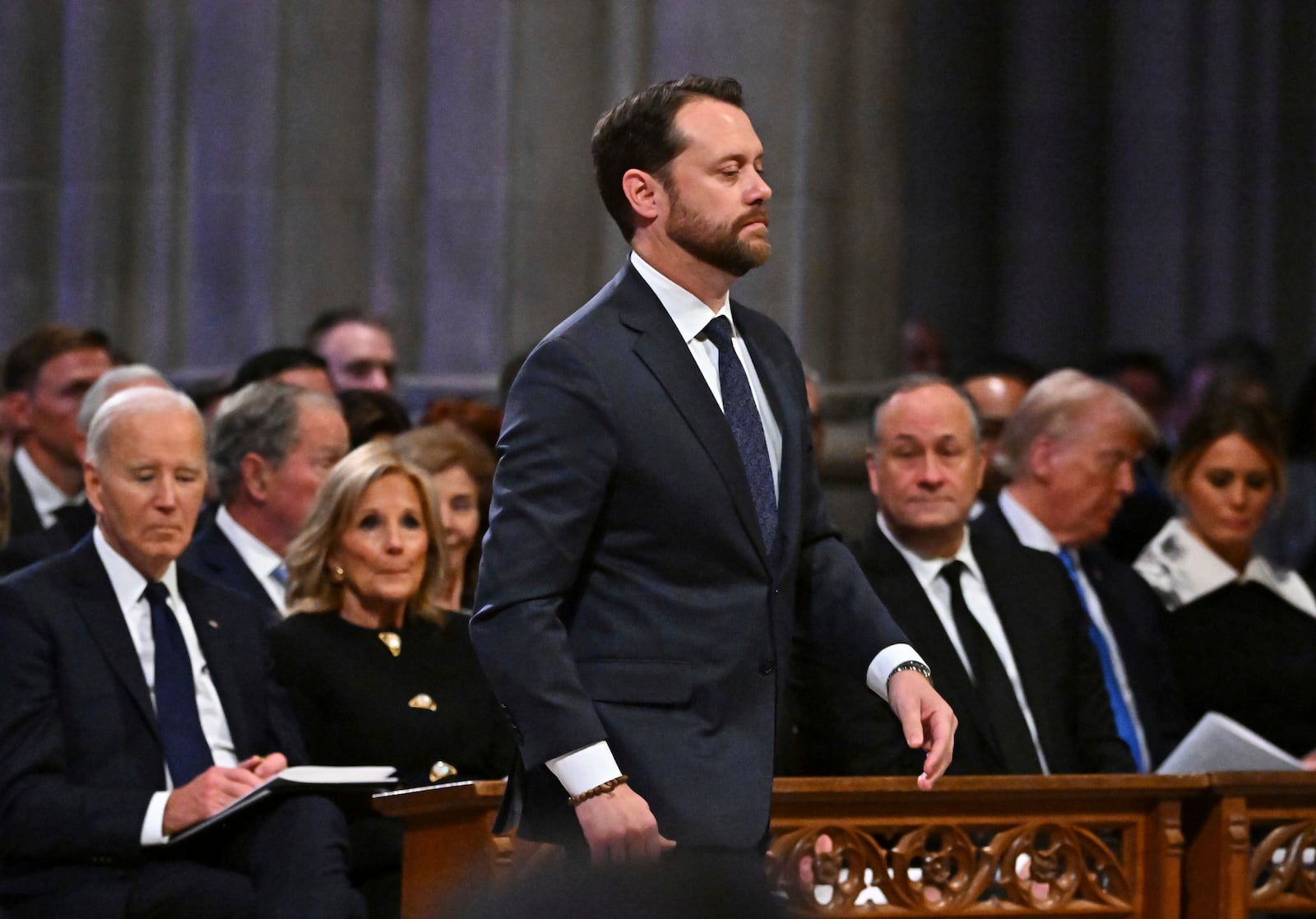 Jason Carter walks to speak during the state funeral for his grandfather former President Jimmy Carter at the National Cathedral, Thursday, Jan. 9, 2025, in Washington. Looking on from left are President Joe Biden, first lady Jill Biden, second gentleman Doug Emhoff, President-elect Donald Trump and his wife Melania Trump. (Ricky Carioti/The Washington Post via AP, Pool)