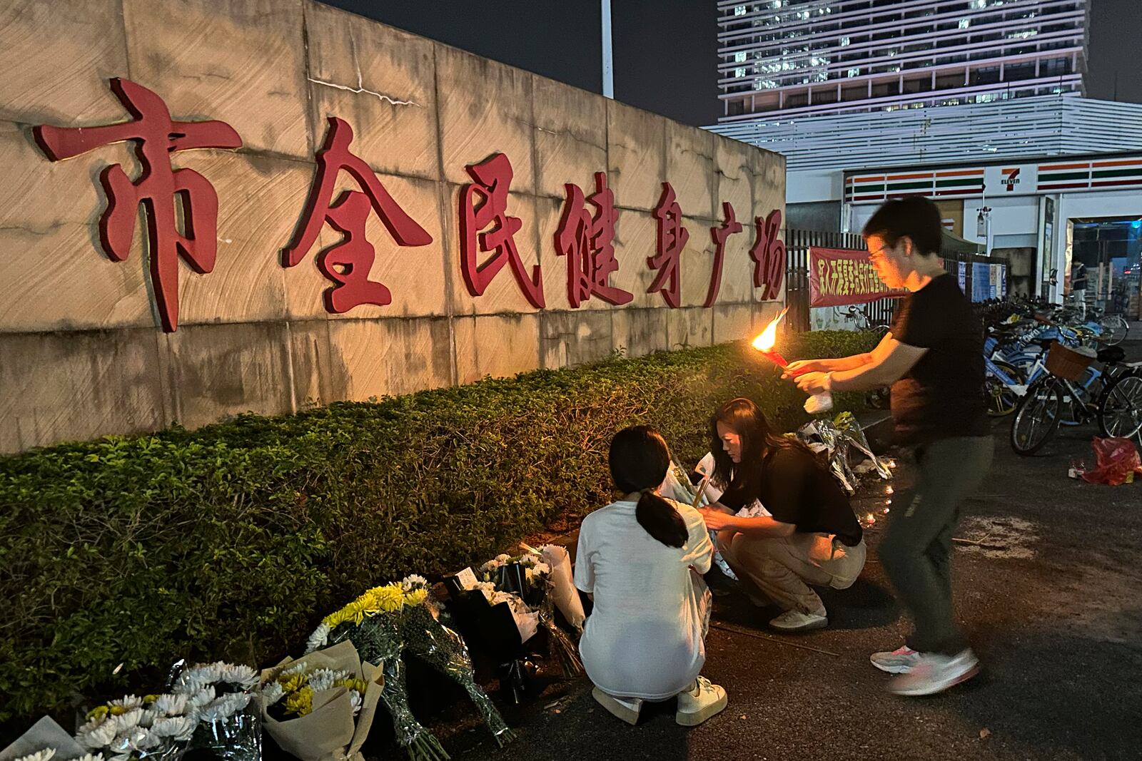 A woman lights a candle as offering near flowers placed outside the "Zhuhai People's Fitness Plaza" where a man deliberately rammed his car into people exercising at the sports center, killing some and injuring others in Zhuhai in southern China's Guangdong province on Tuesday, Nov. 12, 2024. (AP Photo/Ng Han Guan)