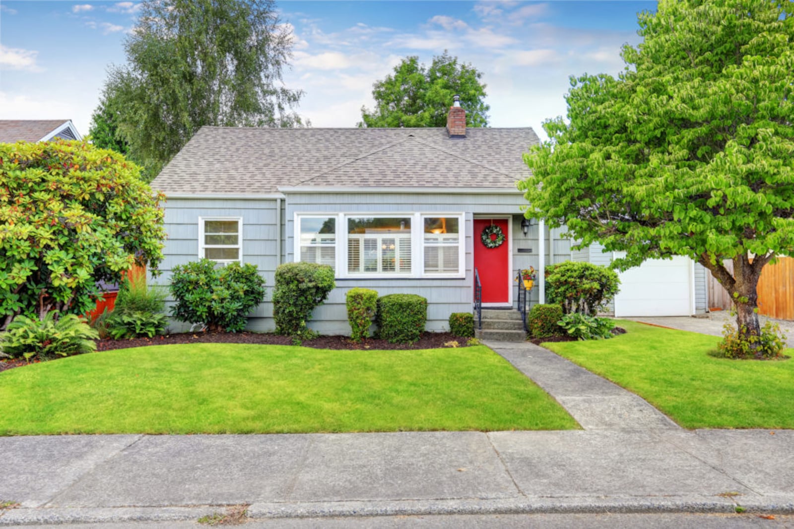 Exterior of small American house with blue paint and red entrance door.