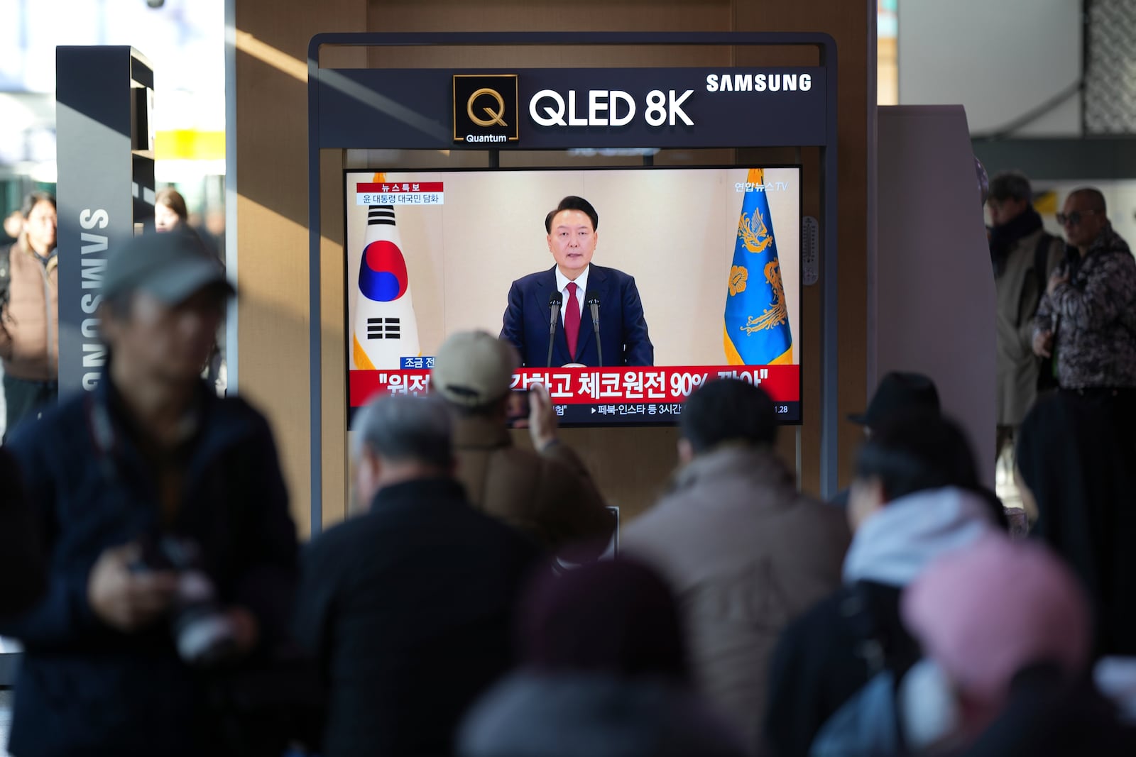 People watch a TV screen showing the live broadcast of South Korean President Yoon Suk Yeol's announcement at the Seoul Railway Station in Seoul, South Korea, Thursday, Dec. 12, 2024. (AP Photo//Lee Jin-man)