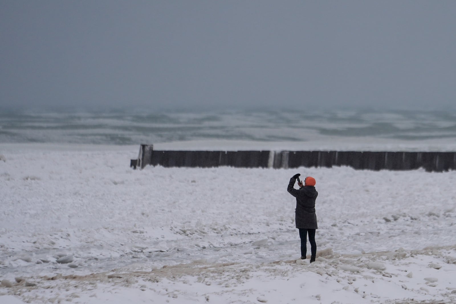 A person takes pictures as they walk on a beach along the shore of Lake Michigan, Wednesday, Feb. 12, 2025, in Chicago. (AP Photo/Kiichiro Sato)