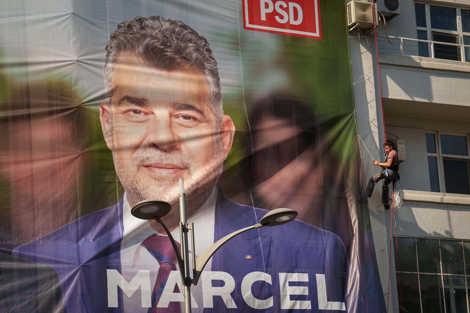 A man installs a large poster of Romanian Prime Minister Marcel Ciolacu, the Social Democratic Party or PSD candidate in the upcoming Nov. 24 presidential elections, in Bucharest, Romania, Friday, Sept. 20, 2024. (AP Photo/Vadim Ghirda)