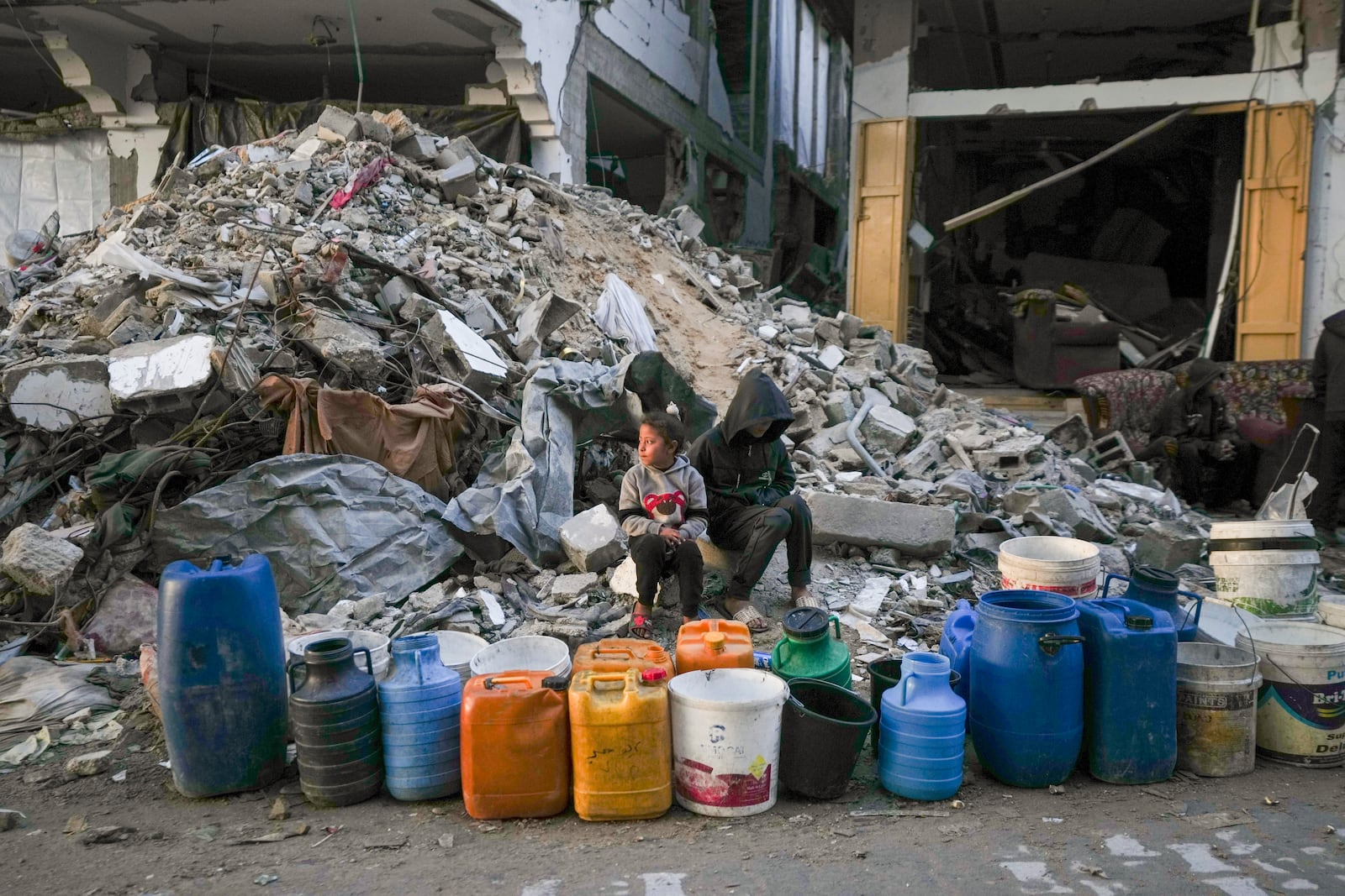 Two children wait to get water next to a line of empty jerrycans in an area largely destroyed by the Israeli army's air and ground offensive in Gaza City, Gaza Strip, Wednesday, Feb. 5, 2025. (AP Photo/Abdel Kareem Hana)