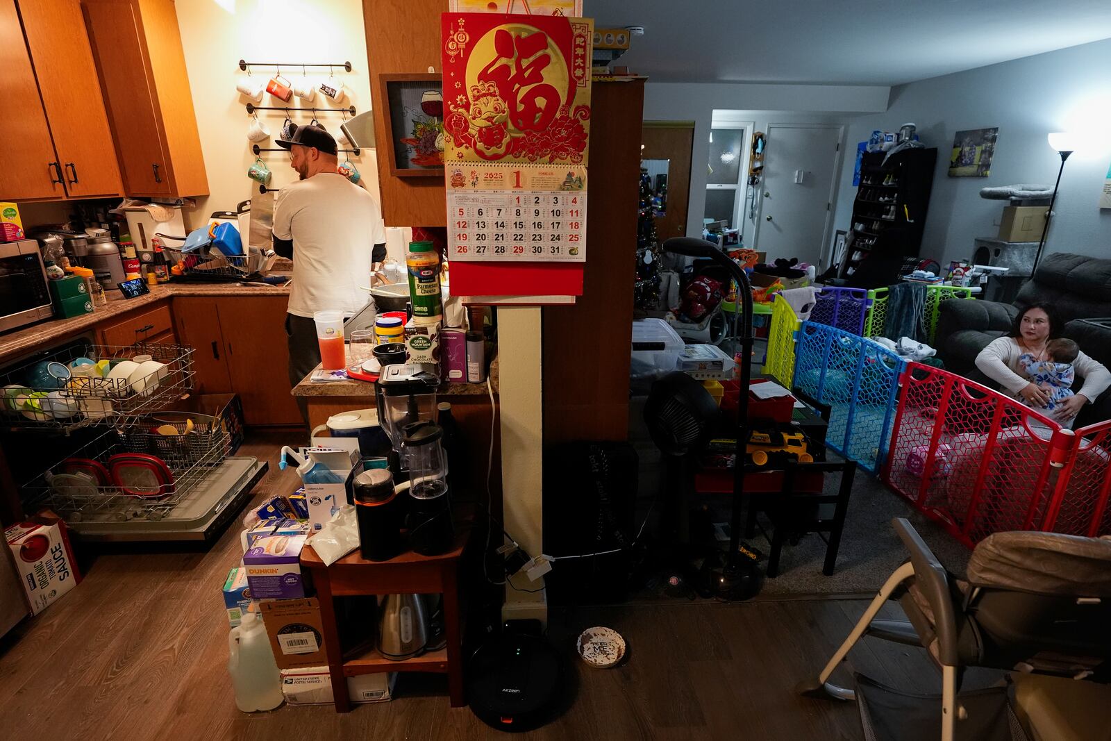 Steve Petersen, left, washes dishes while his wife Jennifer, right, plays with their daughter Carolynn in the living room of their apartment in Campbell, Calif., Wednesday, Jan. 15, 2025. (AP Photo/Godofredo A. Vásquez)