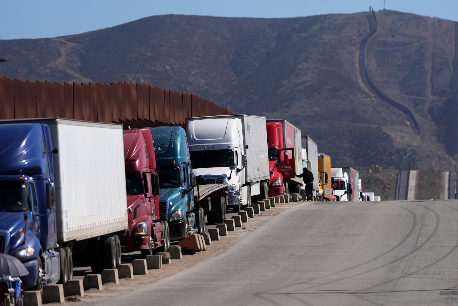 Trucks line up to cross the border into the United States as tariffs against Mexico go into effect, Tuesday, March 4, 2025, in Tijuana, Mexico. (AP Photo/Gregory Bull)