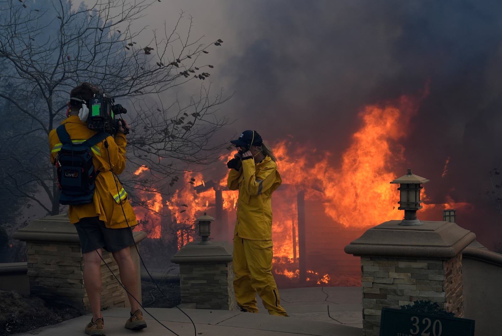 A television crew stands in front of a burning home in the Mountain fire, Wednesday, Nov. 6, 2024, near Camarillo, Calif. (AP Photo/Marcio Jose Sanchez)