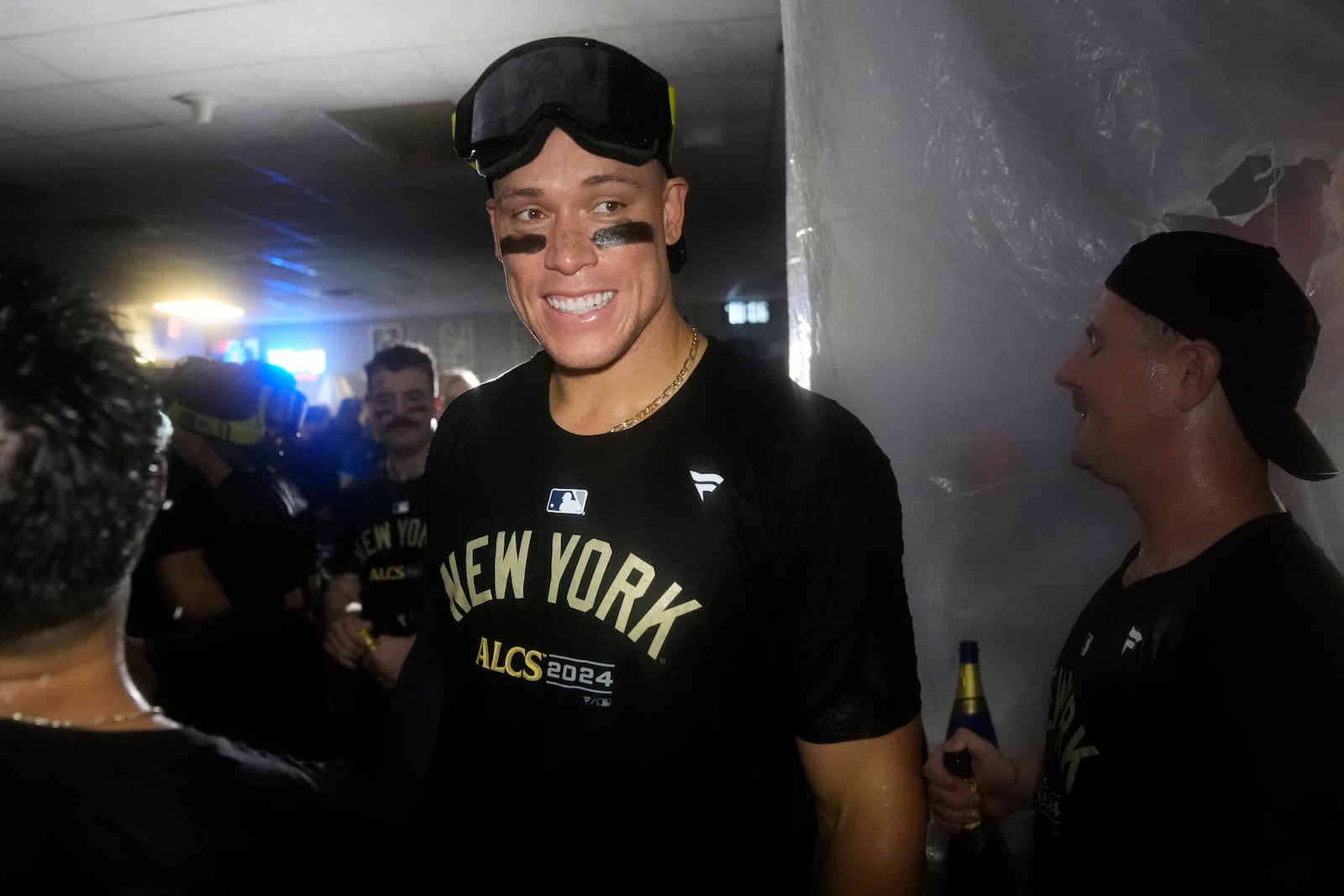 New York Yankees' Aaron Judge celebrates with teammates in the clubhouse following a 3-1 victory over the Kansas City Royals in Game 4 of an American League Division baseball playoff series Thursday, Oct. 10, 2024, in Kansas City, Mo. (AP Photo/Charlie Riedel)