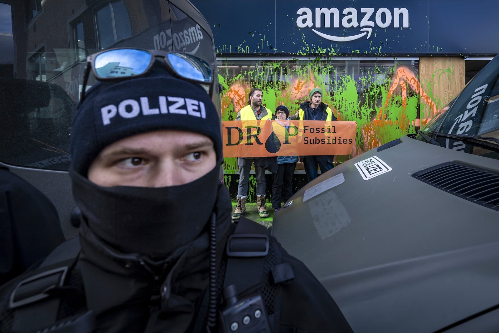 Activists of Drop Fossil Subsidies protest after they sprayed an Amazon shop window with paint as a police officer cordons off the area during the 55th annual meeting of the World Economic Forum, WEF, in Davos, Switzerland, Monday, Jan. 20, 2025. (Michael Buholzer/Keystone via AP)