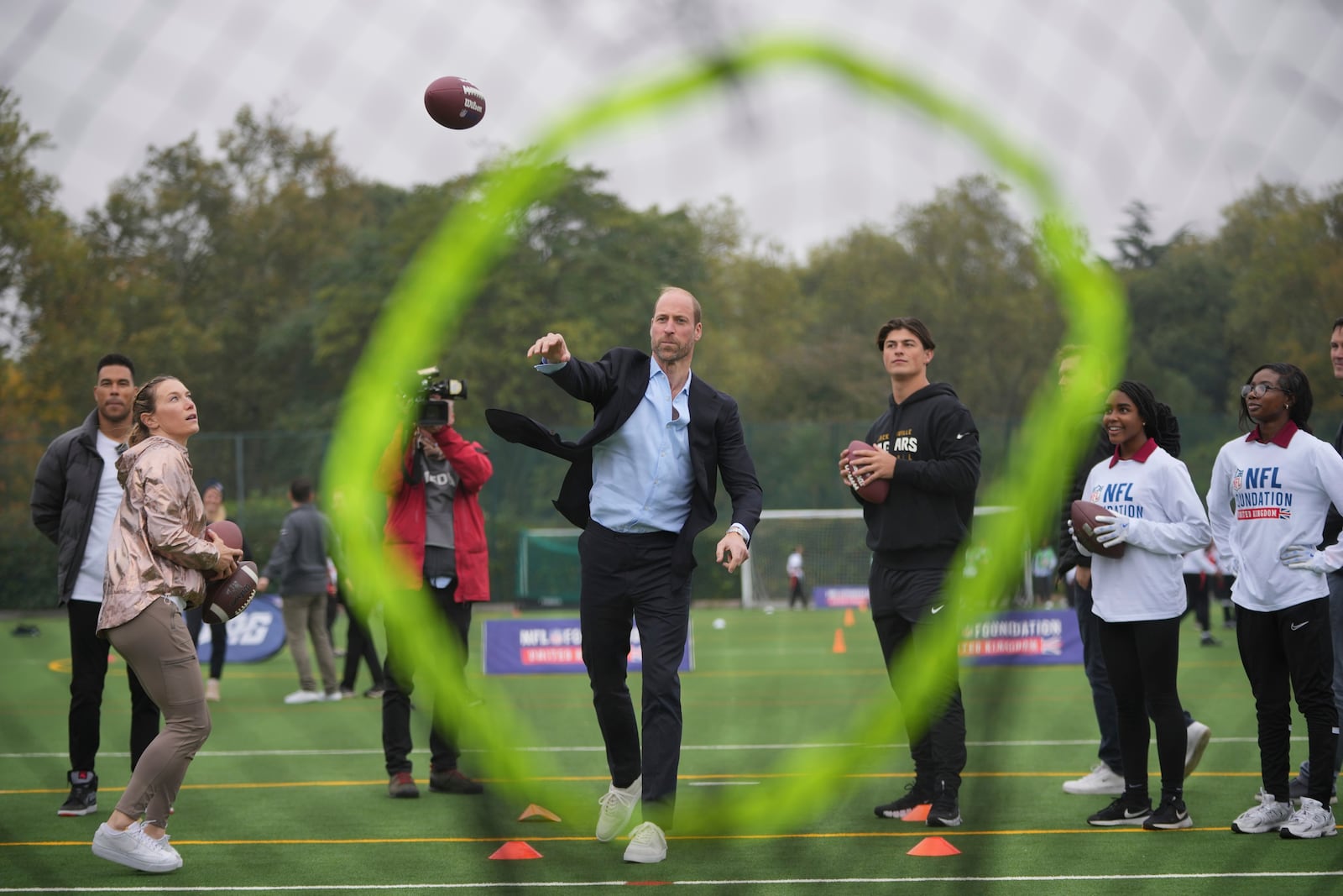 Britain's Prince William throws a football at a target, watched by Louis Rees-Zammit, left, as he attends a NFL Foundation NFL Flag event, an inclusive and fast paced American Football format, in London, Tuesday, Oct. 15, 2024. (AP Photo/Kin Cheung, Pool)