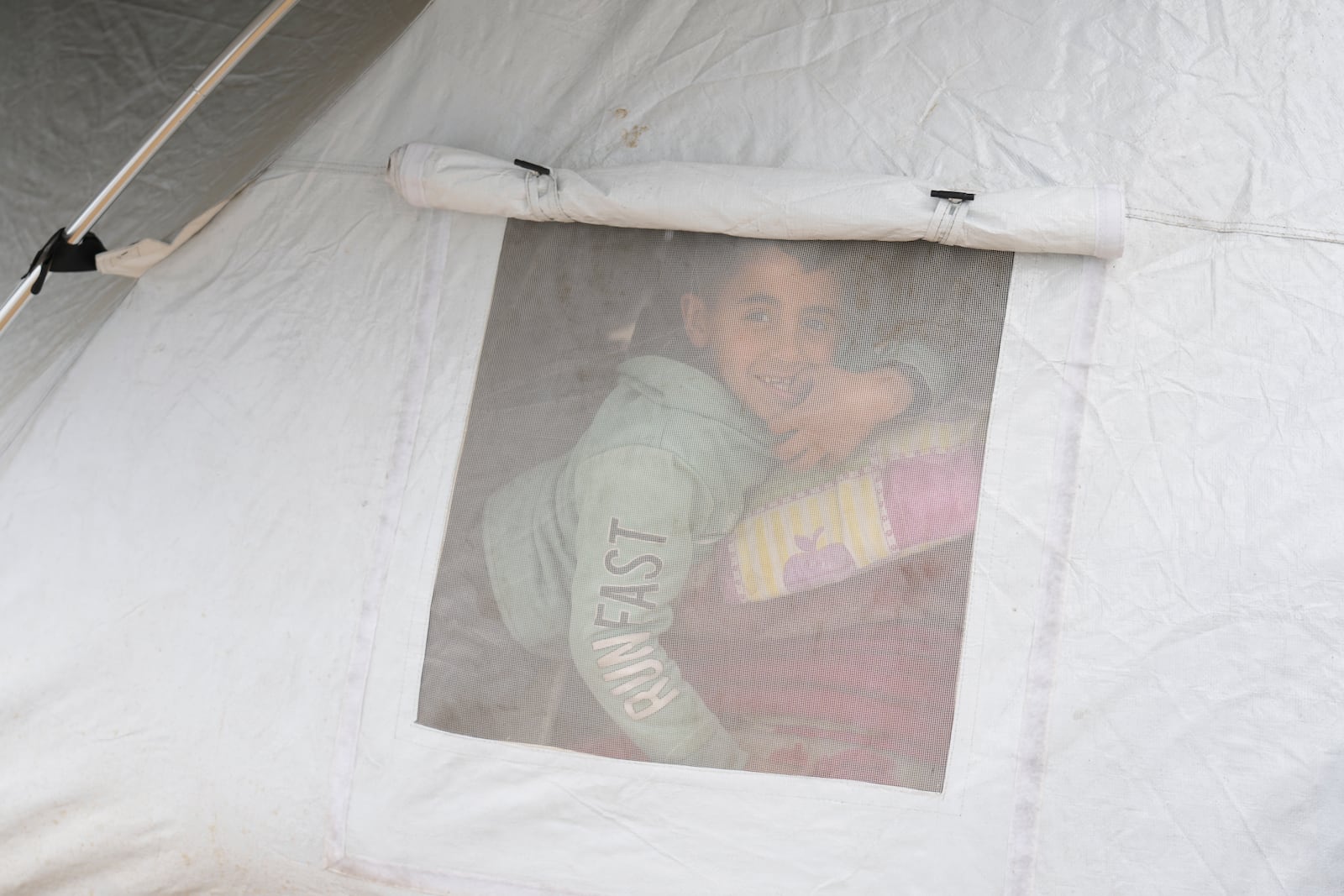 A displaced Palestinian peeks from a tent window in a sprawling camp adjacent to destroyed homes and buildings in Gaza City, Gaza Strip, Saturday, March 1, 2025 during the Muslim holy month of Ramadan. (AP Photo/Abdel Kareem Hana)