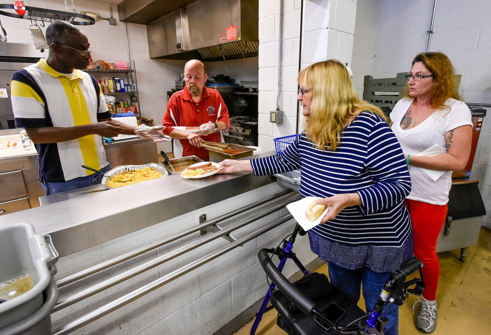 Employee Chris Terry (left) and resident Todd Hammons serve lunch to residents Valeria Abner and Nikki Ketcham on Friday, Nov. 18, at Serve City Chosen Homeless Shelter on East Avenue in Hamilton. The shelter’s 12 women’s beds are all full. NICK GRAHAM/STAFF