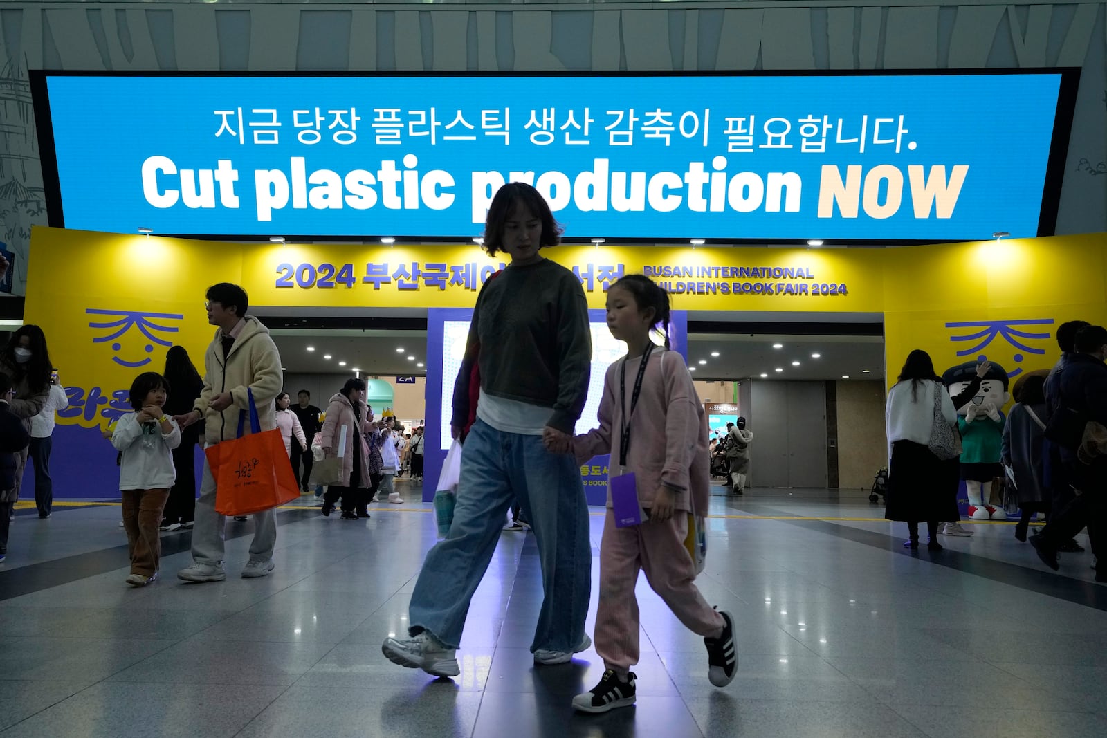 FILE - People pass by a sign calling for a reduction in plastic production near the venue for the fifth session of the Intergovernmental Negotiating Committee on Plastic Pollution in Busan, South Korea, Nov. 30, 2024. (AP Photo/Ahn Young-joon)