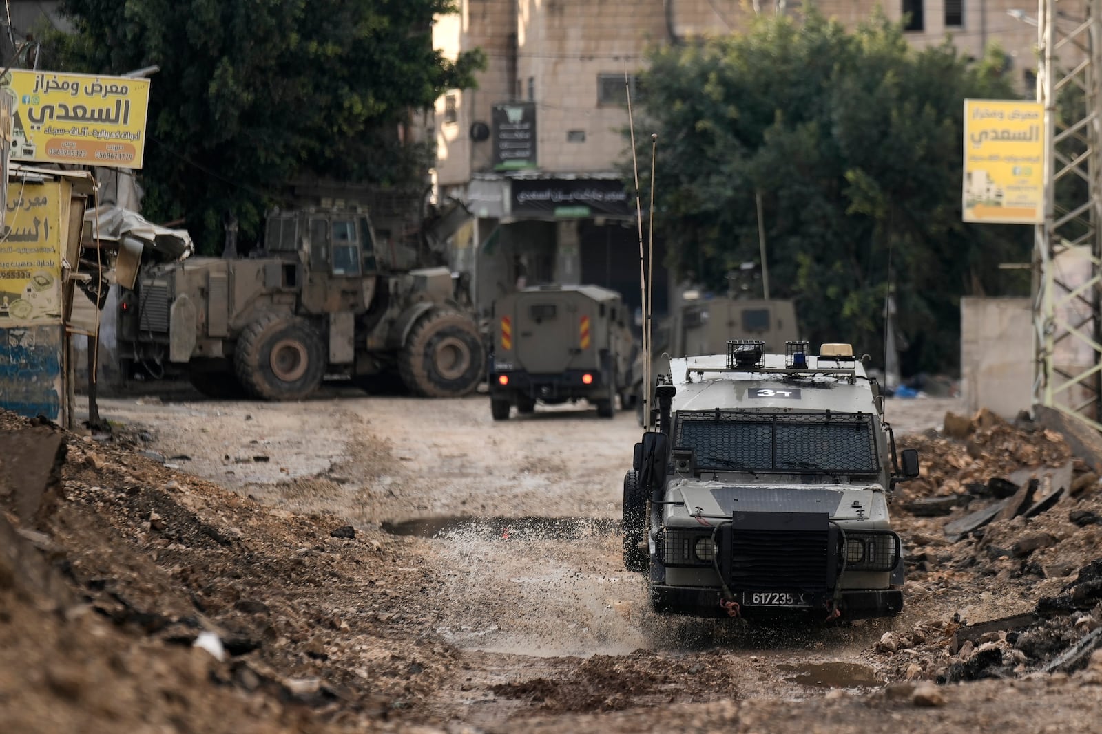 Israeli military vehicles guard a road where a military bulldozer operates in the West Bank refugee camp of Jenin, Tuesday, Nov. 19, 2024. (AP Photo/Majdi Mohammed)