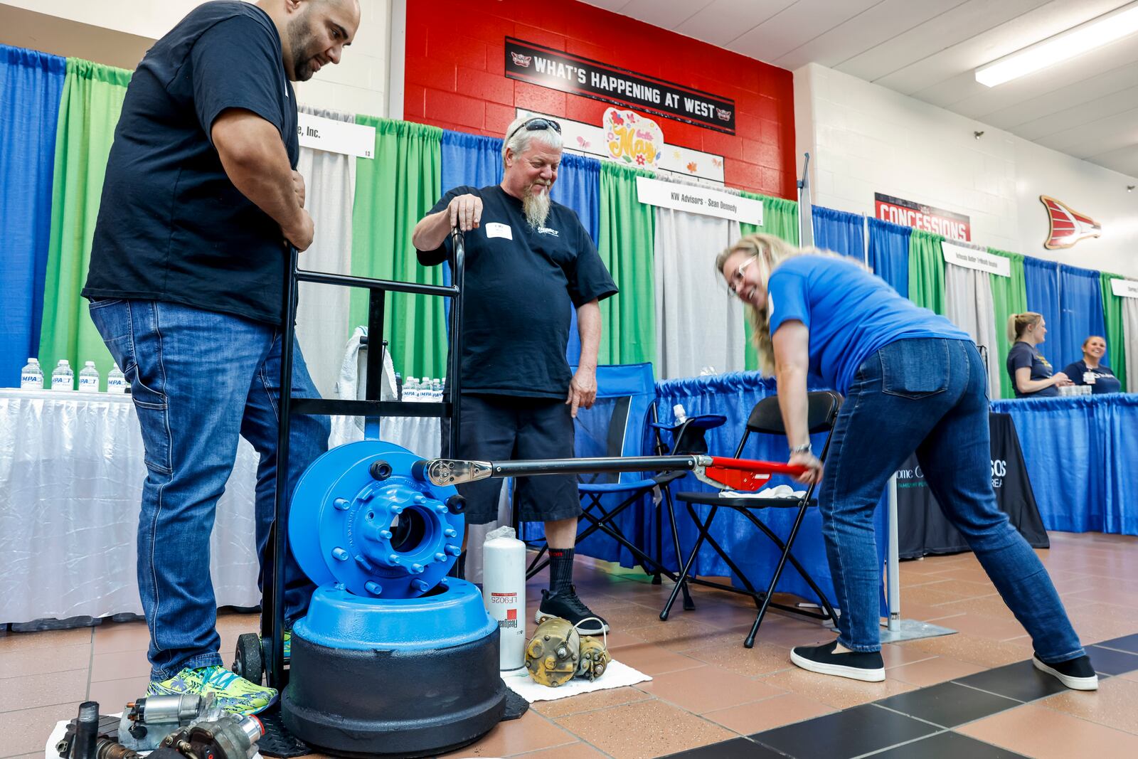 Local businesses and other attendees gathered at Lakota West High School for the West Chester Liberty Chamber alliance Regional Business Expo Tuesday, July 16, 2024 in West Chester Township. Kevin Smith, left, Mark Miller, middle, and Sarah Smith, from Impact Fleet Services, demonstrate how to torque a truck wheel lug nut during the expo. NICK GRAHAM/STAFF