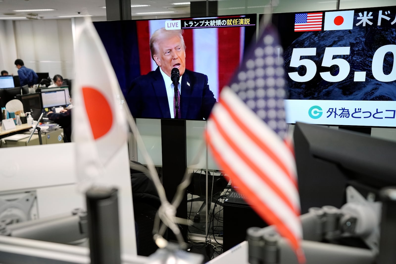 A monitor near a Japanese and the U.S. flags shows Donald Trump delivering a speech at the inauguration ceremony as President of the United States, Tuesday, Jan. 21, 2025, at a foreign exchange trading company in Tokyo. (AP Photo/Eugene Hoshiko)