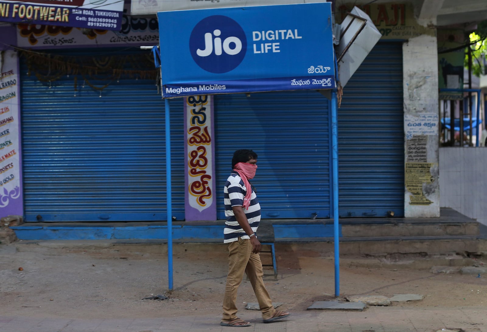 FILE -A man walks past a Reliance Jio signage in front of a closed shop in Hyderabad, India, April 22, 2020 (AP Photo/Mahesh Kumar A, File)