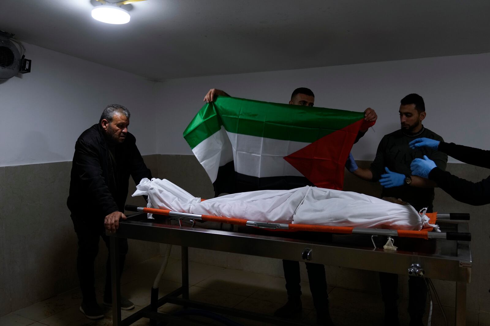 Relatives cover the body of Khalil Al-Saadi, 35, with the Palestinian flag before his funeral, almost two weeks after he was killed in an Israeli army raid, in the hospital morgue in Jenin, West Bank, Sunday, Feb. 2, 2025. (AP Photo/Majdi Mohammed)