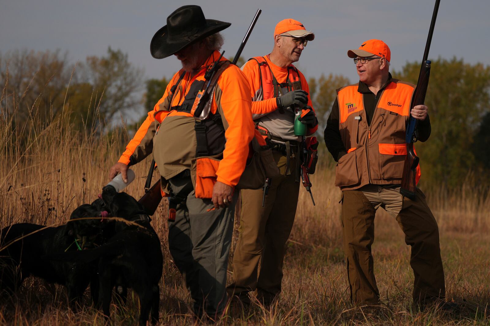 Minnesota Governor and Democratic Vice Presidential candidate Tim Walz talks with Matt Kucharski, as Scott Rall gives water to his three hunting dogs, during the annual Minnesota Governor's Pheasant Hunting Opener, Saturday, Oct. 12, 2024, near Sleepy Eye, Minn. (Anthony Souffle/Star Tribune via AP)