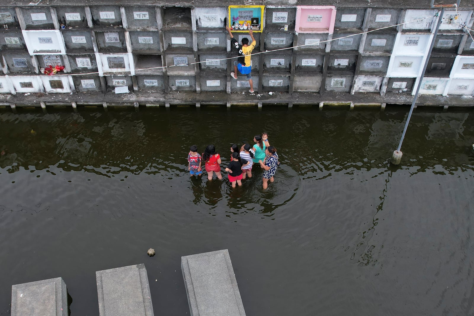 People visit the tomb of family members at flood-prone Holy Spirit Memorial Park in Masantol, Pampanga province, Philippines after heavy rains from recent tropical storm Trami caused water levels to become higher than usual ahead of All Saints Day, Thursday Oct. 31, 2024. (AP Photo/Aaron Favila)