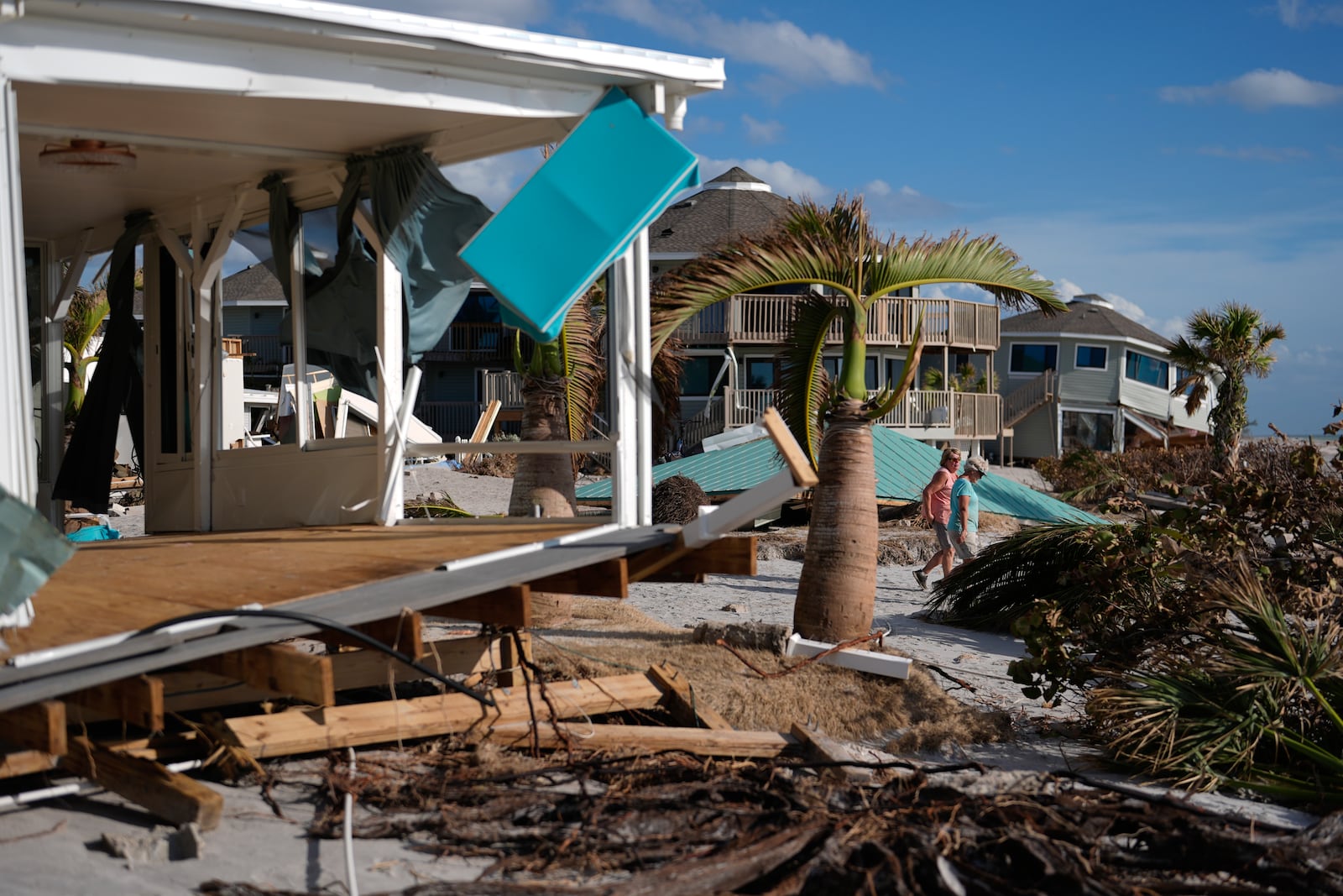 FILE - Resident Kerry Flynn, right, and a friend walk past a damaged home and the displaced roof of their 55+ mobile home community's tiki hut after the passage of Hurricane Milton, on Manasota Key, in Englewood, Fla., Oct. 13, 2024. (AP Photo/Rebecca Blackwell, File)