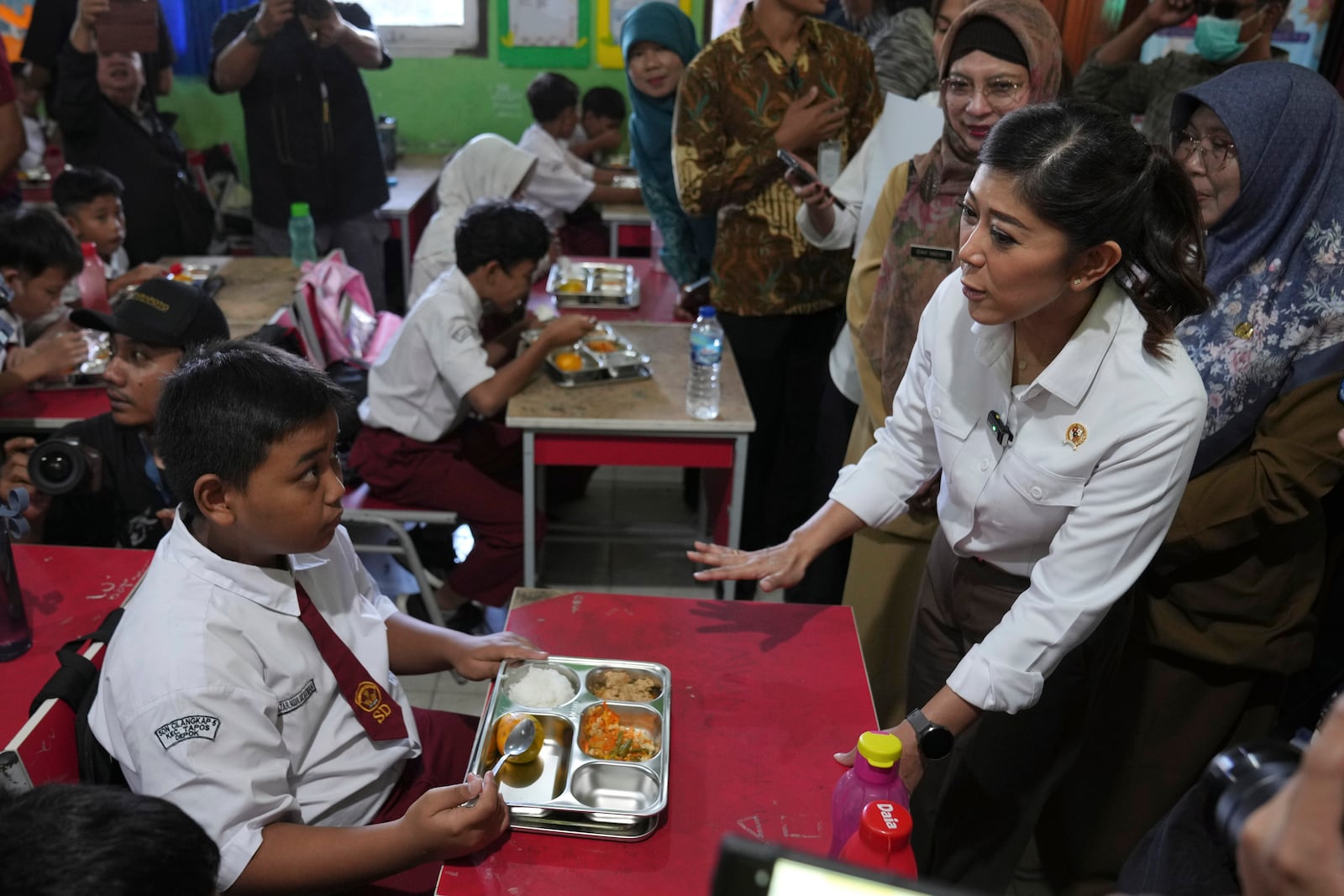 Indonesian Minister of Information and Digital Affairs Meutya Hafid, right, talks to students during the kick off of President Prabowo Subianto's ambitious free meal program to feed children and pregnant women nationwide despite critics saying that its required logistics could hurt Indonesia's state finances and economy, at an elementary school in Depok, West Java, Indonesia, Monday, Jan. 6, 2025. (AP Photo/Dita Alangkara)