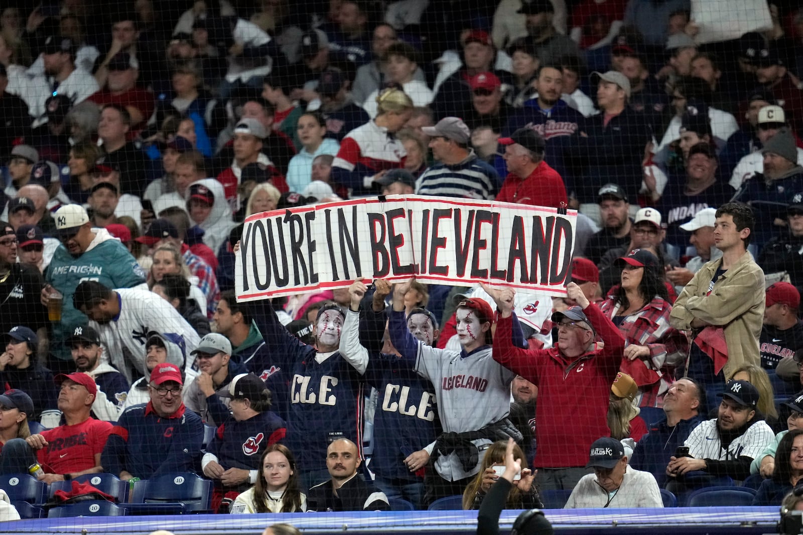 Fans hold up a sign during the second inning in Game 5 of the baseball AL Championship Series between the New York Yankees and Cleveland Guardians Saturday, Oct. 19, 2024, in Cleveland. (AP Photo/Sue Ogrocki)