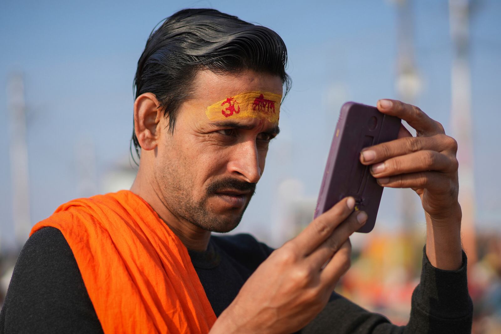 A Hindu devotee looks in the mirror after putting a sacred mark on his forehead at the confluence of the Ganges, the Yamuna, and the Saraswati rivers during the 45-day-long Maha Kumbh festival in Prayagraj, India, Tuesday, Jan. 28, 2025. (AP Photo/Deepak Sharma)