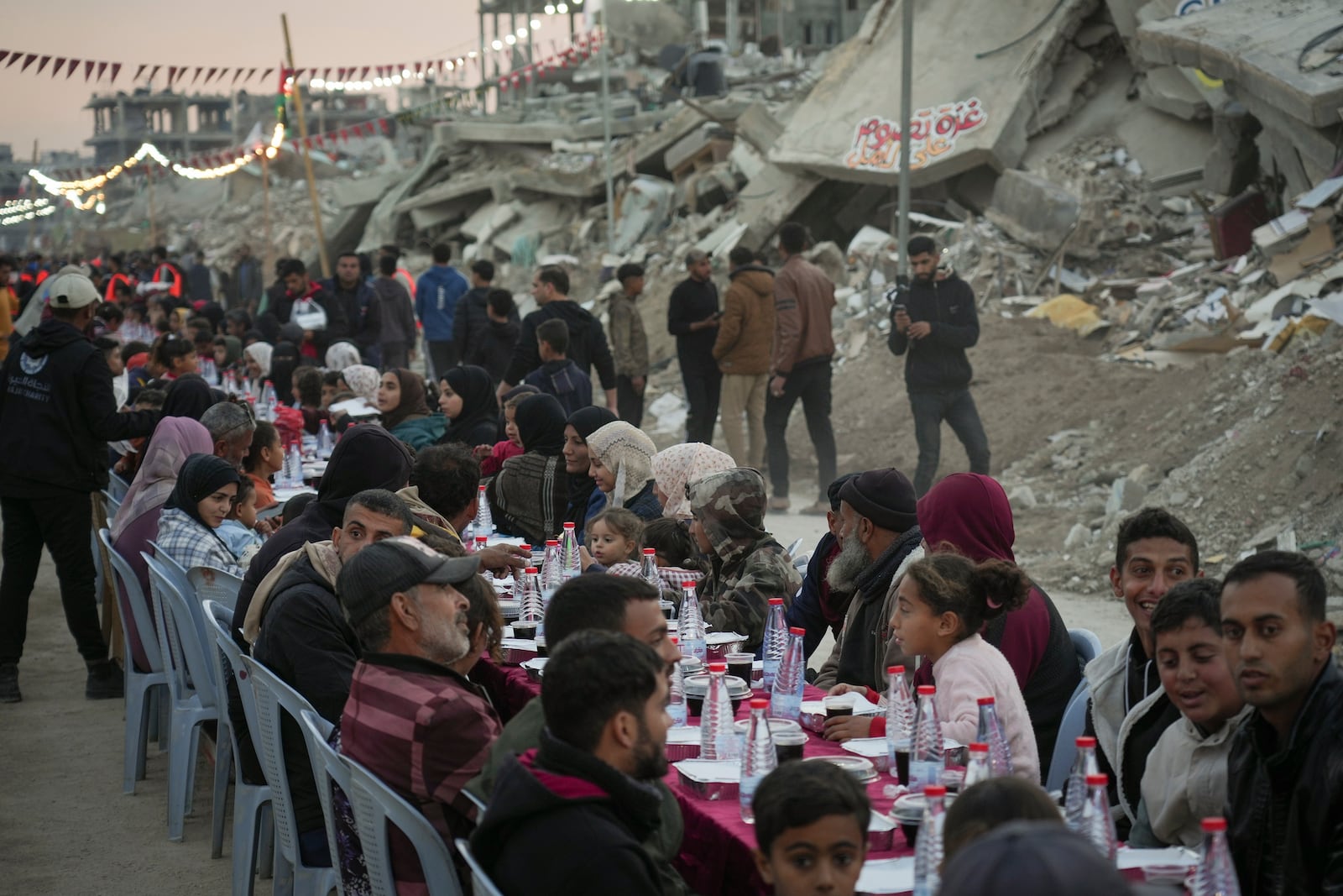 Palestinians sit at a large table surrounded by the rubble of destroyed homes and buildings as they gather for iftar, the fast-breaking meal, on the first day of Ramadan in Rafah, southern Gaza Strip, Saturday, March 1, 2025 (AP Photo/Abdel Kareem Hana)