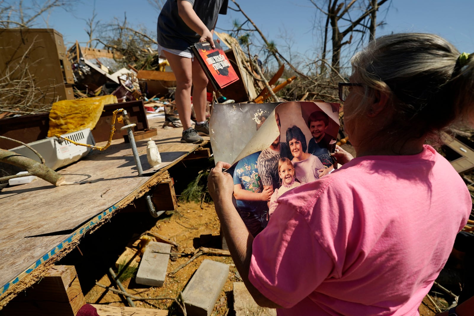 Patricia Blansett inspects a family portrait print, one of the few items that family and friends recovered intact, Sunday, March 16, 2025 from her relative's mobile home that was destroyed when a series of storms passed Tylertown, Miss., on Saturday. (AP Photo/Rogelio V. Solis)