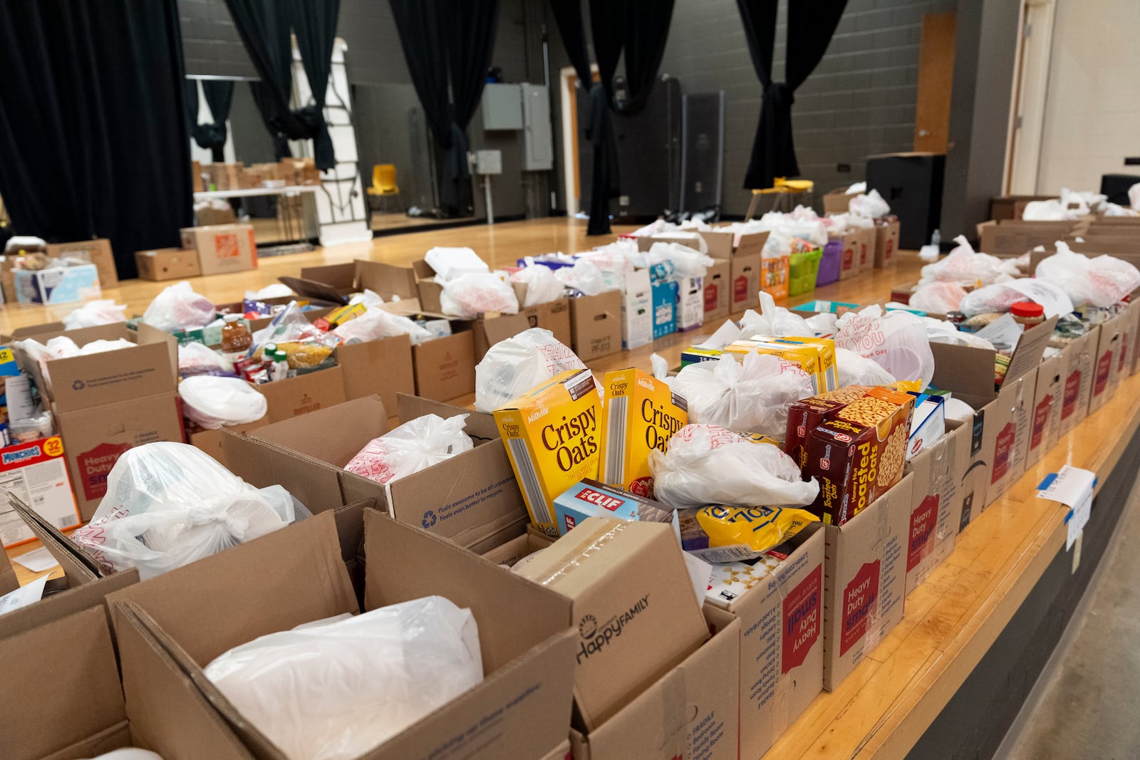 Boxes of food items line the stage in an auditorium of the Dr. Wesley Grant Sr. Southside Community Center in Asheville, N.C., where high school senior Nathan Flaherty volunteers in the aftermath of Hurricane Helene, Wednesday, Oct. 16, 2024. (AP Photo/Stephanie Scarbrough)