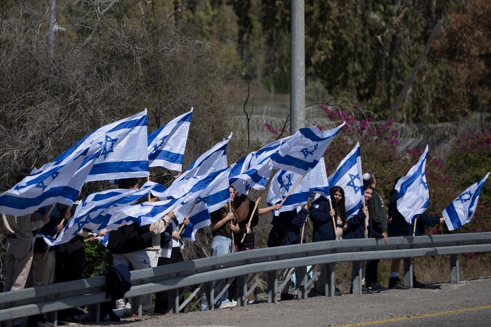 Israelis stand on the side of a road to bid a farewell for the slain hostage Shlomo Mantzur, near the Kibbutz Yad Mordechai, southern Israel, Sunday, March 2, 2025. (AP Photo/Leo Correa)