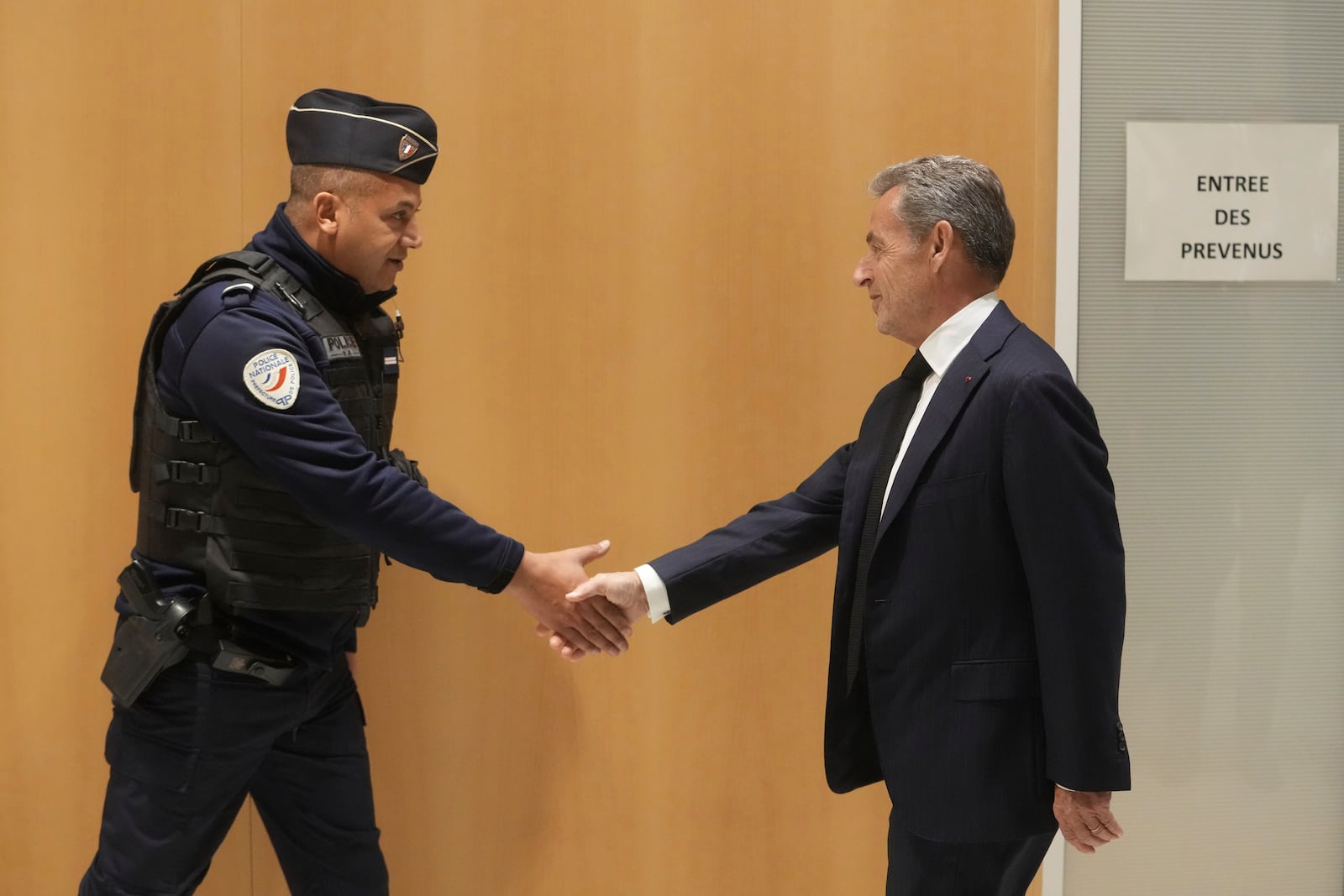 Former French President Nicolas Sarkozy shakes hands to a police officer as he arrives to the courtroom as he goes on trial over alleged illegal financing of his 2007 presidential campaign by the government of late Libyan leader Moammar Gadhafi, Monday, Jan. 6, 2025 in Paris. (AP Photo/Thibault Camus)