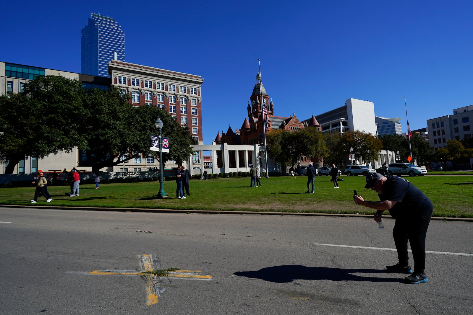 FILE - A person uses a cell phone to capture images of an X on Elm Street at Dealey Plaza, one of two spots marked where President John F. Kennedy was shot, as people gather on the 60th anniversary of his assassination, Nov. 22, 2023, in Dallas. (AP Photo/Julio Cortez, File)