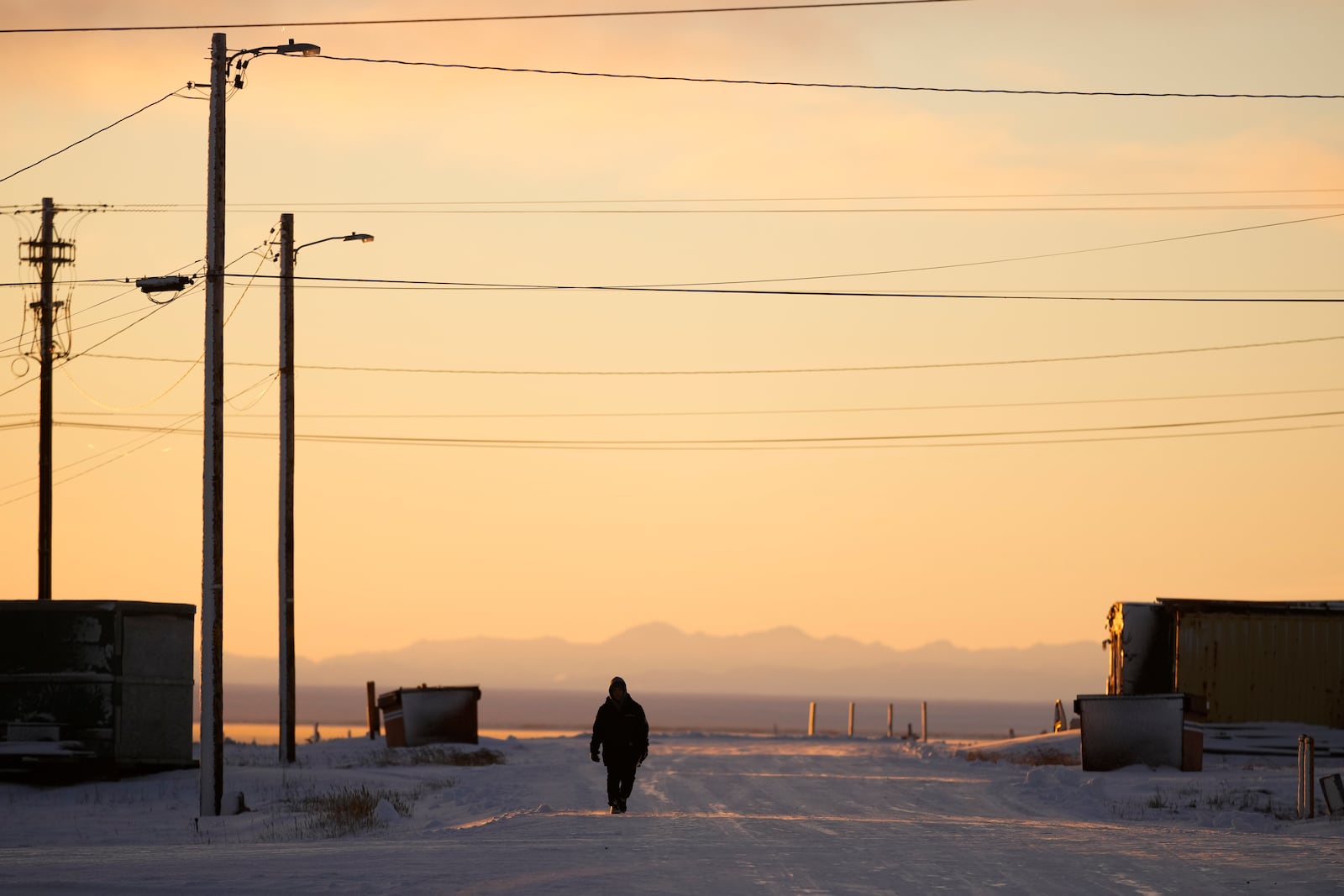 A resident walks up a street as the sun rises Tuesday, Oct. 15, 2024, in Kaktovik, Alaska. (AP Photo/Lindsey Wasson)