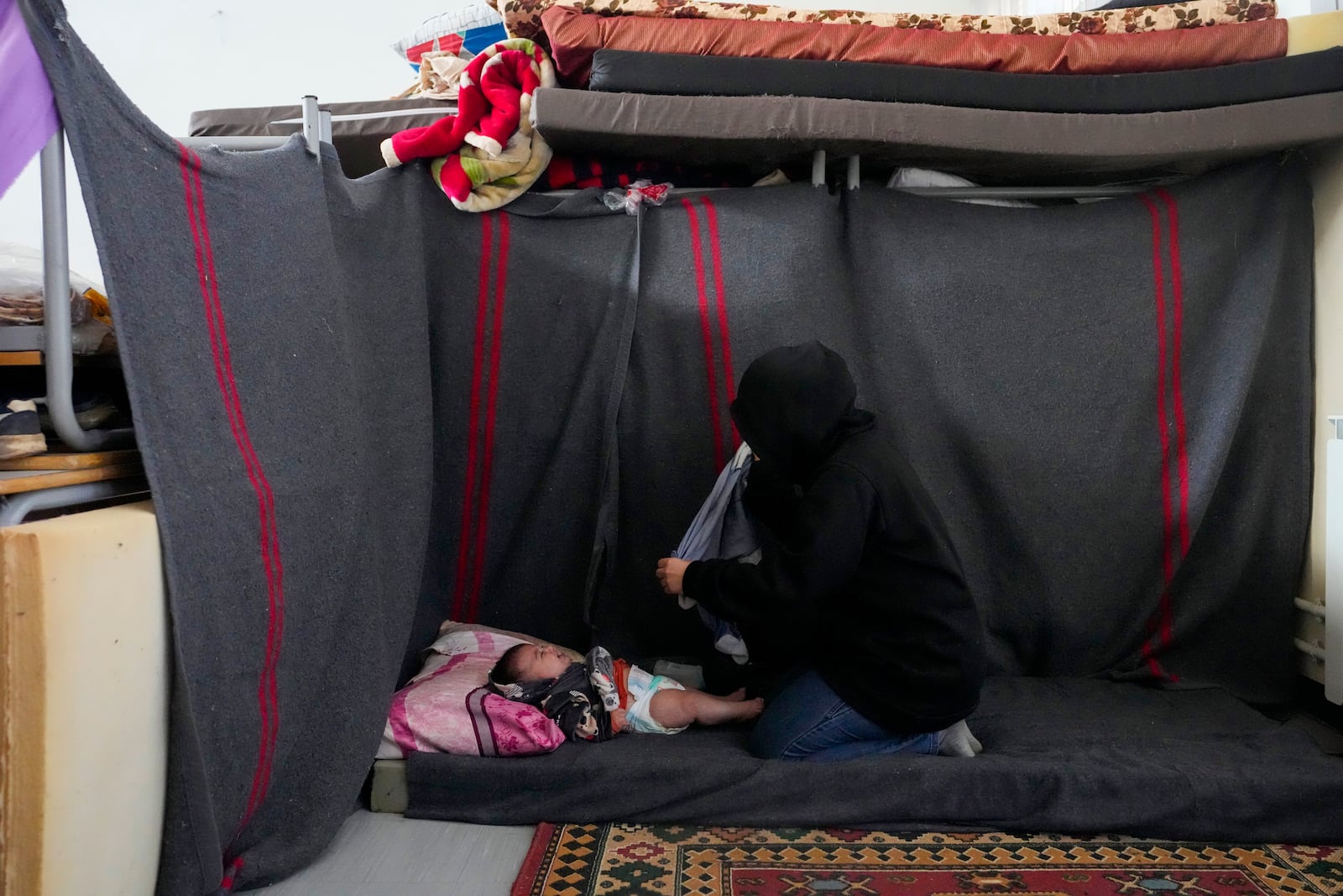 A displaced woman, who fled Baalbek city and the nearby towns of Douris and Ain Bourday amid the ongoing Hezbollah-Israel war, changes the diaper of her daughter at a school being used as a shelter, in Deir Al-Ahmar, east Lebanon, Thursday, Oct. 31, 2024. (AP Photo/Hassan Ammar)