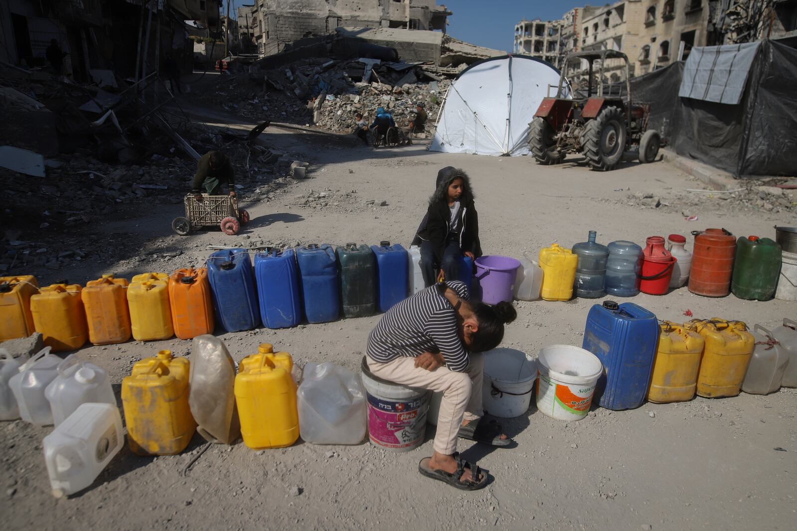 Palestinian children wait next to a row of jerrycans to collect water in Beit Lahia, northern Gaza Strip, Wednesday, Jan. 29, 2025, after Israel began allowing hundreds of thousands of Palestinians to return to the heavily damaged area last Monday.(AP Photo/Jehaid Alshrafi)