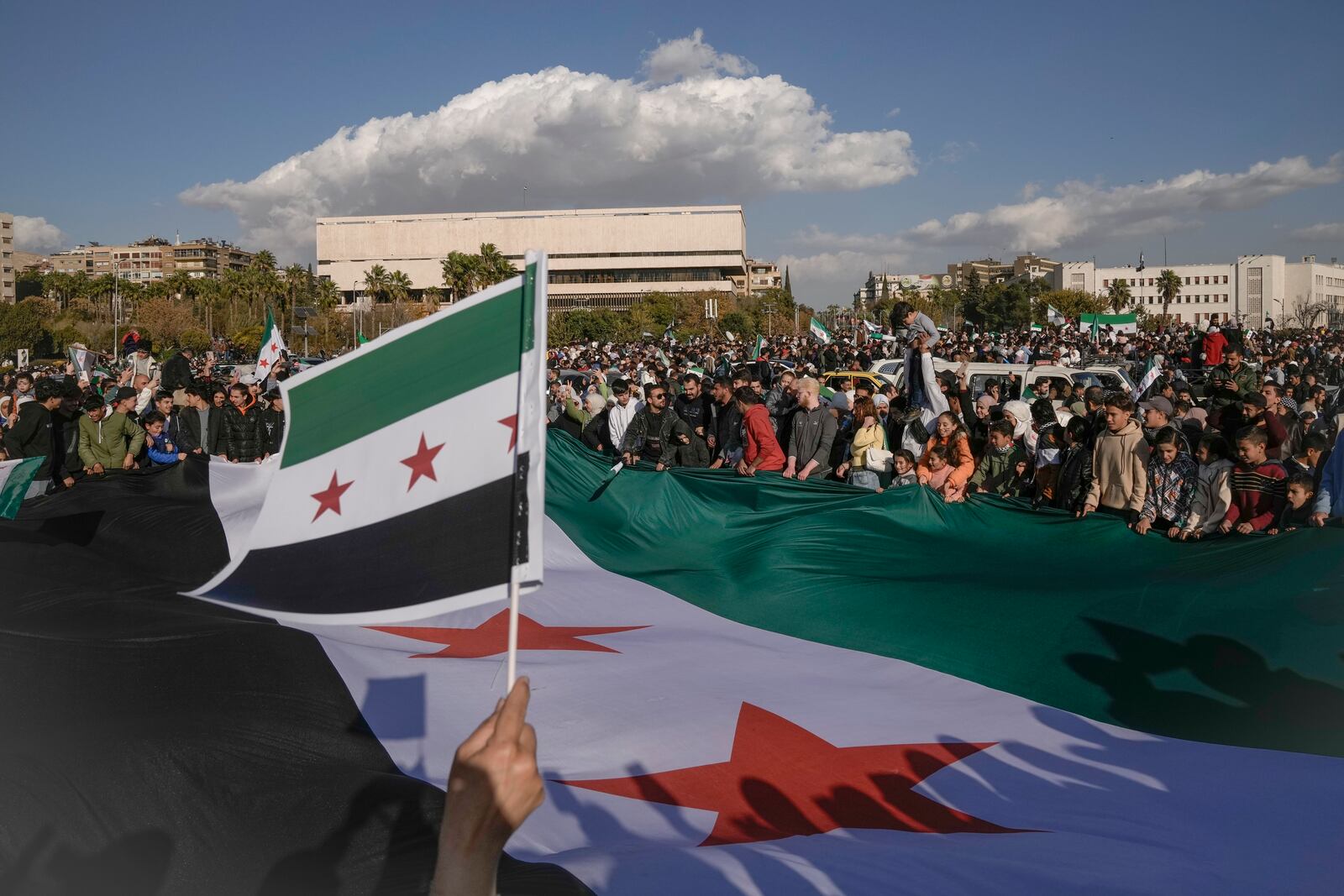 Syrians display a giant "revolutionary" Syrian flag during a celebratory demonstration following the first Friday prayers since Bashar Assad's ouster, in Damascus' central square, Syria, Friday, Dec. 13, 2024. (AP Photo/Leo Correa)