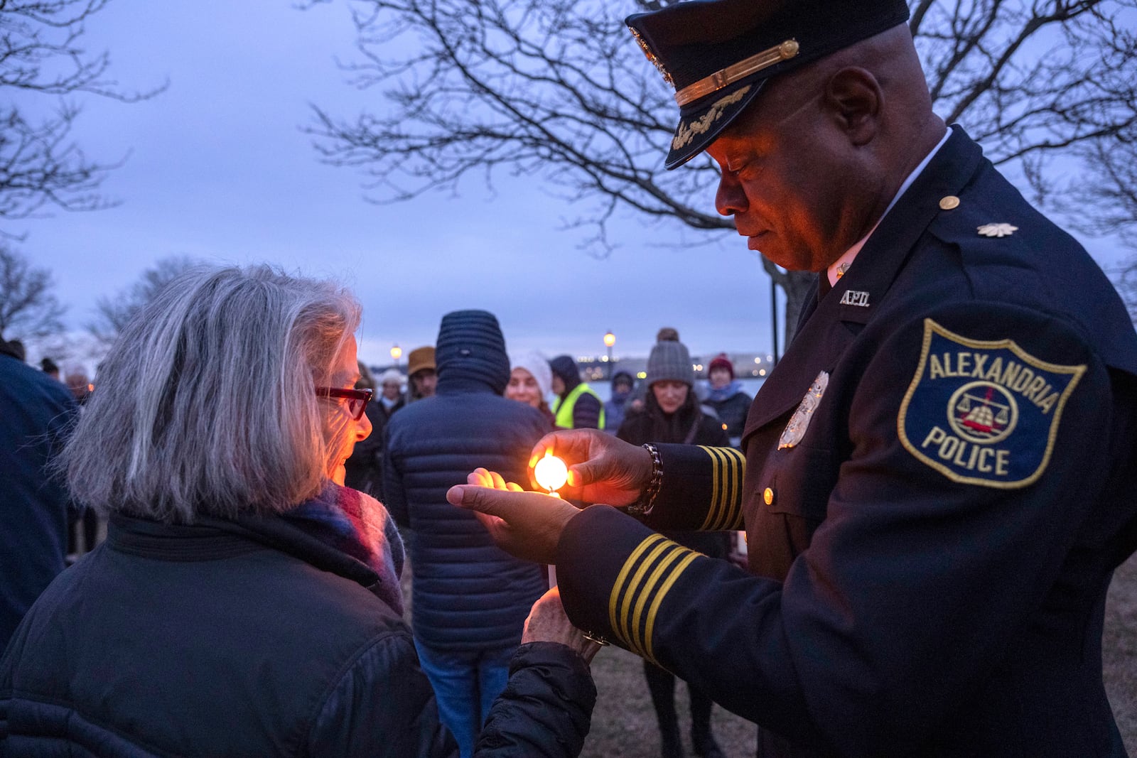 Krista Oberlander, left, helps light the candle of Assistant Police Chief for the City of Alexandria Easton McDonald at the start of a candlelight vigil, Wednesday, Feb. 5, 2025, in Alexandria, Va., for the victims of the mid-air collision of an American Airlines jet and a Black Hawk helicopter at Reagan National Airport. (AP Photo/Kevin Wolf)