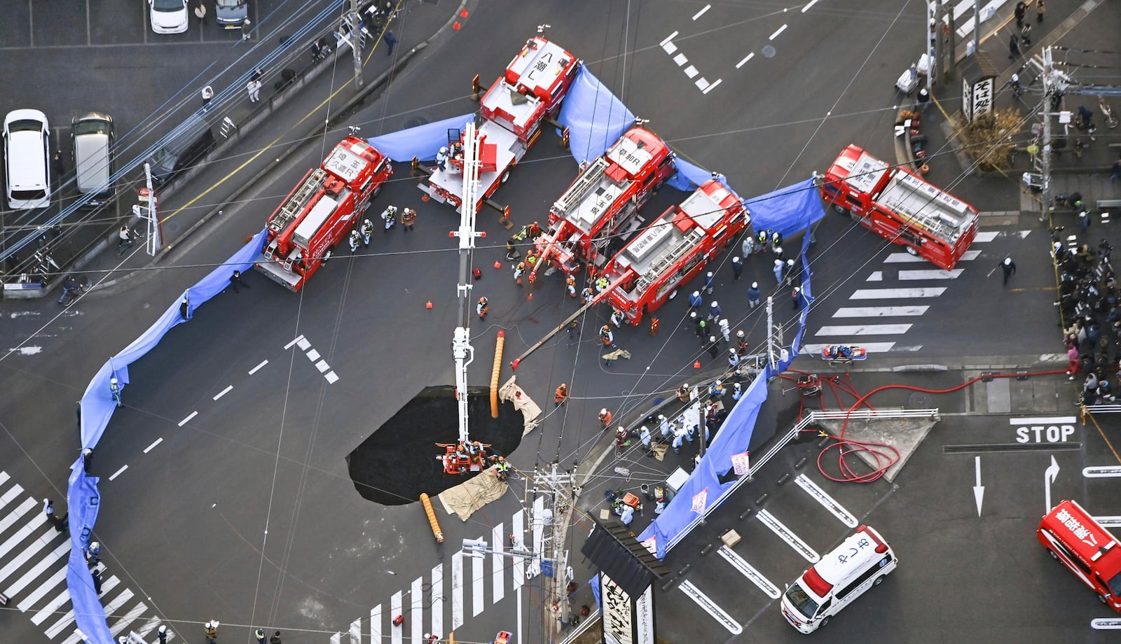 First responders try to rescue the driver of a truck that fell into a sinkhole on a street in Yashio, northeast of Tokyo, Tuesday, Jan. 28, 2025. (Kenichiro Kojima/Kyodo News via AP)