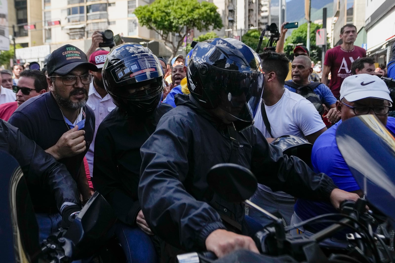 Opposition leader Maria Corina Machado, wearing a helmet at left, sits on the back of a motorcycle as she is driven away after addressing people at a protest against President Nicolas Maduro in Caracas, Venezuela, Thursday, Jan. 9, 2025, the day before his inauguration for a third term. (AP Photo/Matias Delacroix)