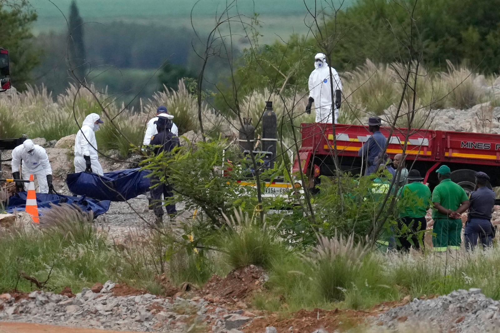 Forensic service workers carry bodies in blue body bags during a rescue operation to rescue miners from below ground in an abandoned gold mine in Stilfontein, South Africa, Wednesday, Jan. 15, 2025. (AP Photo/Themba Hadebe)