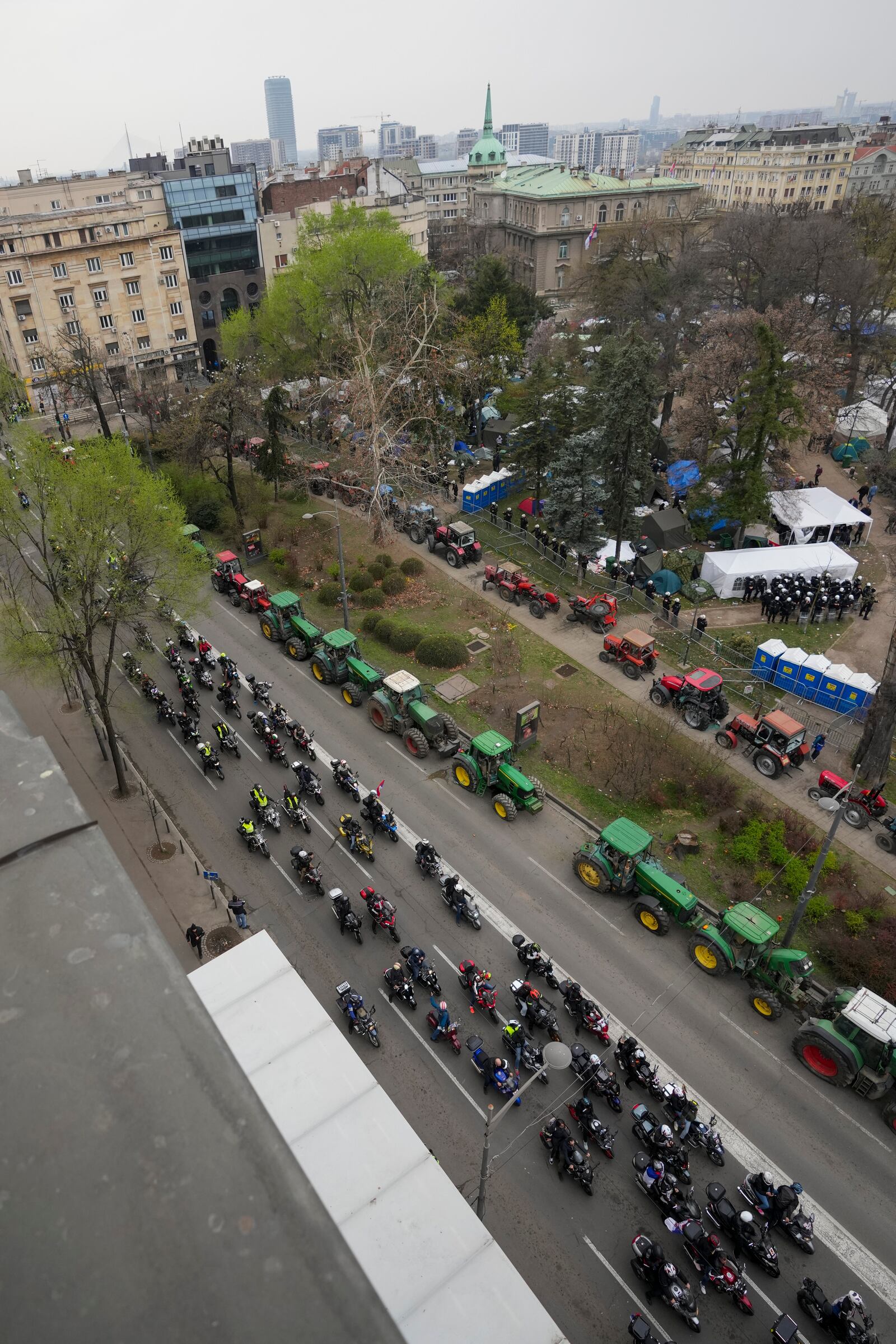 Bikers ride by a students and former paramilitary fighters, loyal to President Aleksandar Vucic, camp outside the presidency building prior a major anti-corruption rally in downtown Belgrade, Serbia, Saturday, March 15, 2025. (AP Photo/Darko Vojinovic)