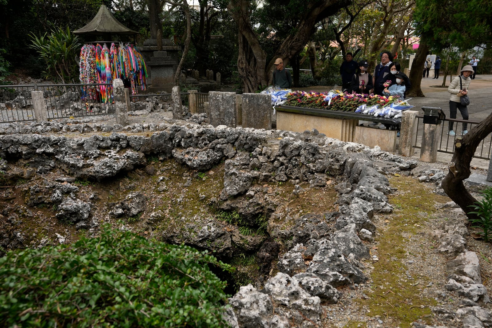 Visitors bring flowers and pray at the "Himeyuri" cenotaph, not seen, created by a cave in Itoman, on the main island of the Okinawa archipelago, southern Japan, Friday, Feb. 14, 2025, as they visit the Himeyuri peace museum that commemorates the Himeyuri female student corps who died during the Battle of Okinawa towards the end of the World War II in 1945. (AP Photo/Hiro Komae)