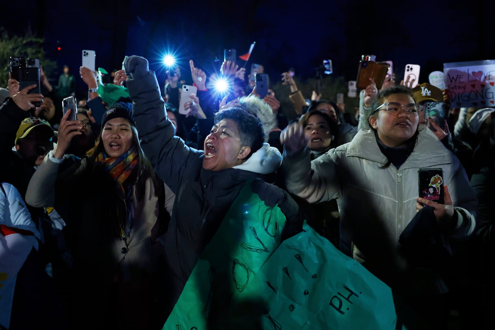 Supporters of former Philippine President Rodrigo Duterte hold up their phones and wave banners during a demonstration outside the International Criminal Court detention center near The Hague in Scheveningen, Netherlands, Wednesday, March 12, 2025. (AP Photo/Omar Havana)