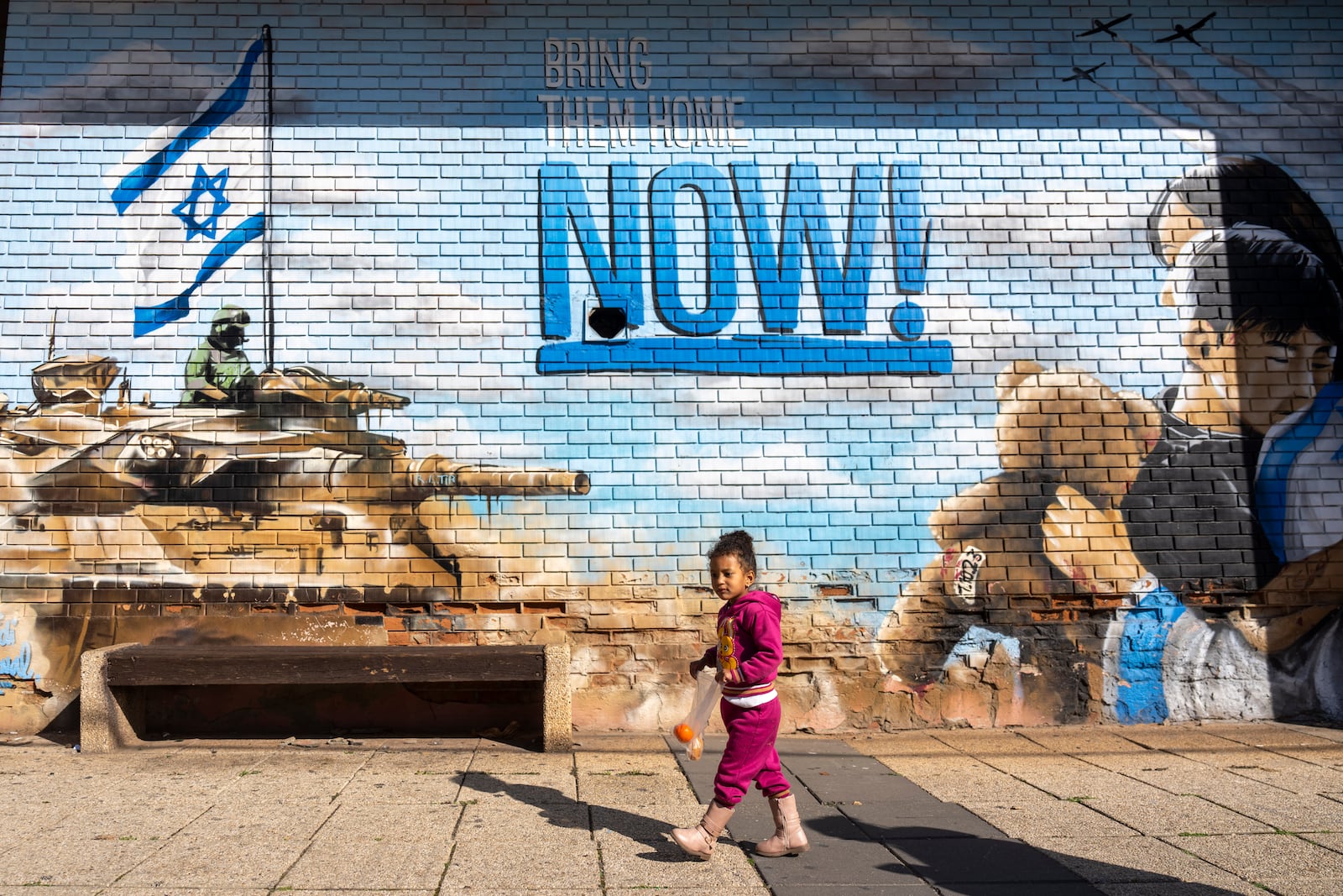 A girl walks past a graffiti, calling for the return of the hostages kidnapped during the Oct. 7 , 2023 Hamas cross-border attacks in Israel, in Kfar Saba, Israel, Sunday, Jan. 19, 2025. (AP Photo/Ariel Schalit)